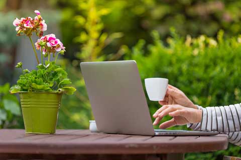 Person sitting at a garden table designing a garden border, using garden design software on a laptop.